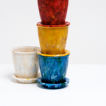 A group of Buoy's eco-friendly Deco rounded plant pots, made of recycled marine plastic waste, with a white one on the left and three — blue, yellow and red — stacked to its right. Made in Japan from waste collected in Japan, and on display at NiMi Projects UK.