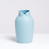 A large blue-gray Ceramic Japan x Nendo Dress Up porcelain vase, shaped like a rotund figure with a wing-tip collar at its neckline on display at NiMi Projects UK.