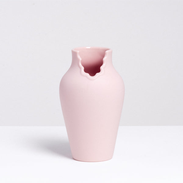 A pink porcelain vase that appears like a figure with a scalloped dress neckline, made by Ceramic Japan and designed by Nendo, displayed on a white background at NiMi Projects UK.