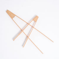 Two pairs of bamboo serving tongs, made in Japan, each with triangular tops. A 18 cm pair with ridged ends is on top of a longer 30 cm pair with grooved ends. On show at NiMi Projects UK.