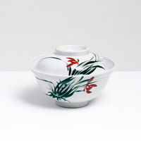 A vintage Japanese ceramic donburi (rice dish) lidded bowl in white, with a hand-painted wild orchid design of green leaves and red flowers on its side and lid. On display at NiMi Projects UK.