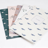 A collection of Japanese notebook covers featuring different motifs. Clockwise from top left — dinosaurs on green, poodles on pink, butterflies on grey, polar bears on white, and whales on ivory white.