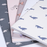 A collection of Japanese notebook covers featuring different motifs. Clockwise from top left — dinosaurs on green, poodles on pink, butterflies on grey, polar bears on white, and whales on ivory white.