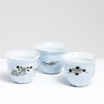 A group of three vintage Arita-yaki, Japanese porcelain cups, on show at NiMi Projects UK, each in pale-blue translucent glaze and decorated with hand-painted motifs in gold. One features a peony with swirls, another a pheasant and the last with chrysanthemums.