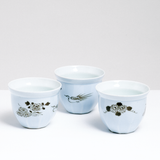 A group of three vintage Arita-yaki, Japanese porcelain cups, on show at NiMi Projects UK, each in pale-blue translucent glaze and decorated with hand-painted motifs in gold. One features a peony with swirls, another a pheasant and the last with chrysanthemums.
