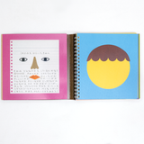 The Kokuyo Face Sticker book, open to show two pages on display at NiMi Projects UK. On the left page is an illustration of a sheet of writing paper with a pair of eyes, a brown nose and a red mouth, while on the right-hand page is a blank face template with wavy brown hair.