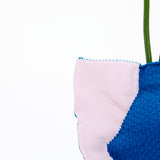 A closeup of the top right corner of a NiMi Projects' Moheim Silhouette knitted vase cover, showing a pink edge and blue center. 
