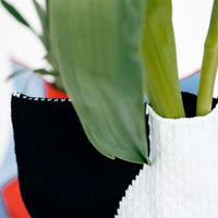 A closeup of a top corner of a NiMi Projects' Moheim Silhouette knitted vase cover, showing a navy blue edge and white center. 