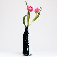 A side view of a Moheim Silhouette jersey knit vase cover available at NiMi Projects UK, featuring a white silhouette of a vase on a navy blue background and stretched over a bottle holding two pink tulips.