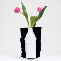 A Moheim Silhouette jersey knit vase cover available at NiMi Projects UK, featuring a white silhouette of a vase on a navy blue background and stretched over a bottle holding two pink tulips.
