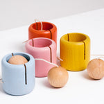 Four NiMi Projects wooden Ototama Cup and Ball toys, a kendama like game, with cups in blue, pink, orange and yellow, and each with a natural ball.