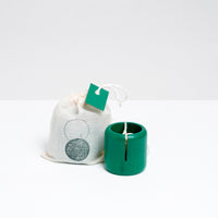 A green Ototama Cup and Ball toy, displayed next to a NiMi Projects cotton bag. The toy is a kendama-like game of a cup and a natural colored ball that’s attached to its center by a white cord.