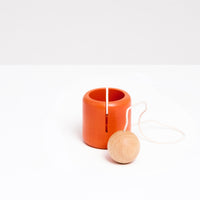 An NiMi Projects orange Ototama Cup and Ball game. This toy is a Japanese kendama-like game featuring a cup and a natural colored ball that’s attached to its center by a white cord.