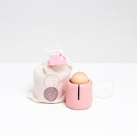 A pink wooden Ototama Cup and Ball toy, displayed with a NiMi Projects bag. The toy is a kendama-like game featuring a cup and a natural colored ball, attached by a white string