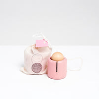 A pink wooden Ototama Cup and Ball toy, displayed with a NiMi Projects bag. The toy is a kendama-like game featuring a cup and a natural colored ball, attached by a white string