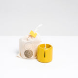 A yellow Ototama Cup and Ball toy, displayed next to a NiMi Projects cotton bag. The toy is a Japanese kendama-like game of a cup and a natural colored ball that’s attached to its center by a white cord.
