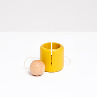 An Ototama Cup and Ball toy, displayed with a NiMi Projects bag. The toy is a kendama-like game with a yello cup and a natural colored ball, attached by a white string