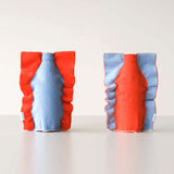 Two Moheim Silhouette vases, displayed side by side to show both sides of the product. The knitted vase features a silhouette of a bottle in sky blue on an orange background on one side, and an orange silhouette on a sky blue background on the other.