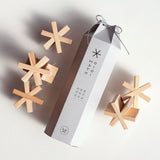 Six Sukima Hositoshi wood star-shaped, asterisk-like building blocks, arranged around their hexagonal, grey paper card storage box, tied at the top with a drawstring. Made in Japan and available at NiMi Projects UK