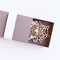 Three Sukima snowflake Christmas ornaments, laser cut in Japanese Shina wood and packaged in a grey cardboard box, sold at NiMi Projects UK.