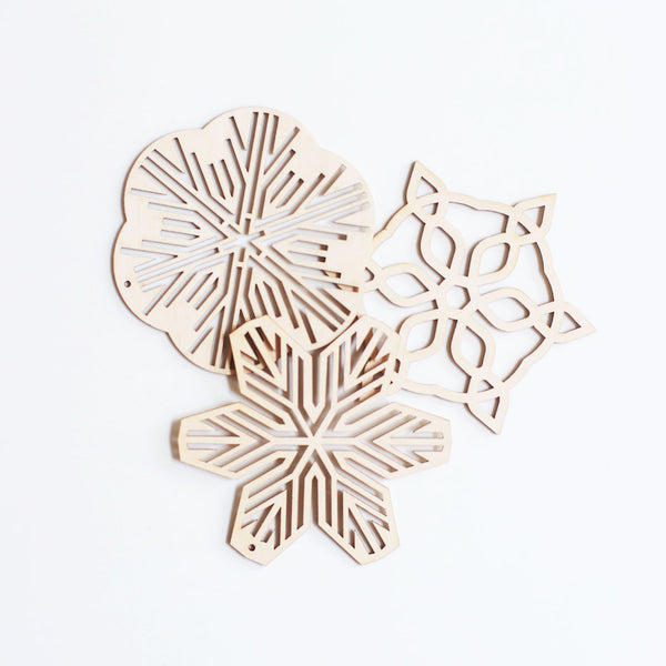 Three Sukima Japanese Shina wood snowflake Christmas ornaments, laid flat slightly overlapping each other, available at NiMi Projects UK 