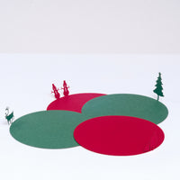 Four laser-cut circular paper coasters, two red and two green, featuring silhouettes of a deer, a pair of snowmen, a Santa Claus, and a Christmas tree, one on each the edge of a circle and folded up to appear standing. Designed by Terada-Mokei and on show at NiMi Projects UK. 