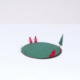 Four stacked red and green paper laser-cut circular coasters, each featuring a different silhouette of a figure on their edges, folded up to appear standing and surrounding the circles. Figures include a Santa Claus, a Christmas tree, a pair of snowmen and a deer. On show at NiMi Projects UK