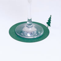 A green circular laser-cut paper coaster, designed by Terada-Mokei, featuring a Christmas tree silhouette on the edge, which is folded up to be standing. Available at NiMi Projects UK.