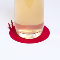 A red laser-cut paper coaster, designed by Terada-Mokei, featuring the silhouettes of a pair of snowmen on the edge, folded up to appear standing on the edge of the circle. Available at NiMi Projects UK. 