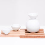 A Japanese porcelain sake set, served on a Hinoki (Japanese Cypress) and Cherry wood slatted trivet made in Japan by Tosa Ryu, and available at NiMi Projects UK.