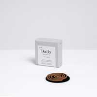 A grey cardboard box of  Trunk Design Japanese Daily Uzumaki outdoor incense coils, with one of its brown incense spirals placed infront on a black heatproof mat. Made on Awaji island in Japan and available at NiMi Project  UK