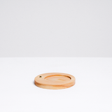 A circular wood incense stand, with an indent for a heatproof mat for paper incense and a side hole for traditional Japanese stick incense, designed by Trunk Design in Japan and available at NiMi Projects UK.