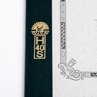 A close up of the gold embossed initials HS and swallow logo on the spine of a Japan-made Tsubame Swallow Notebook, available at NiMi Projects UK.