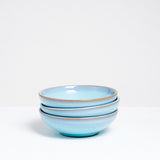 A side view of three stacked small blue vintage Japanese ceramic round bowls.