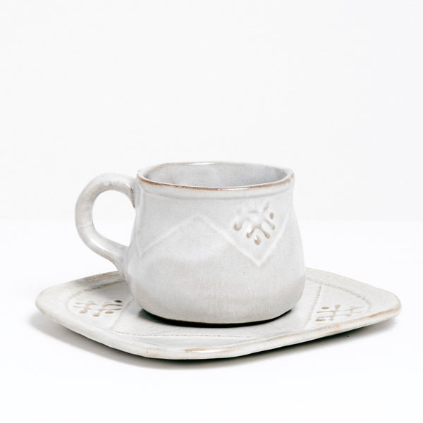 A white vintage handmade Japanese ceramic coffeecup and saucer, featuring a raised design of a zigzag across the cup body and criss-cross motifs.