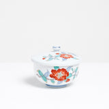 Side view of a white vintage Japanese porcelain lidded tea cup, featuring a design of hand painted red peonies and blue and green leaves.