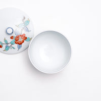 Top view of a white vintage Japanese porcelain lidded tea cup, featuring a design of hand painted red peonies and blue and green leaves.