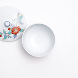 Top view of a white vintage Japanese porcelain lidded tea cup, featuring a design of hand painted red peonies and blue and green leaves.