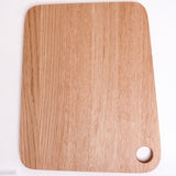 A small rhomboid oak wood bread board with a hole to hang it by in the bottom left, made in Japan by Atelier Yocto and available at NiMi Projects UK.