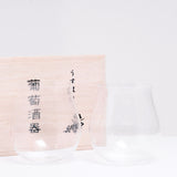 A pair of clear Shotoku Usuhari extra-thin Japanese stemless wine glasses with rounded bottoms and tulip-wine-glass tops, displayed at NiMi Projects UK in front of their paulownia box packaging.