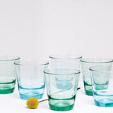 Six Toyo Sasaki Glass Spash stackable glass tumblers in transparent green and blue, displayed on a white background at NiMi Projects UK.
