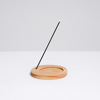 A circular wooden incense stand, with a circle indent for a heatproof mat for paper incense, and a side hole holding a stick of traditional Japanese incense, made in Japan by Trunk Design and available at NiMi Projects 