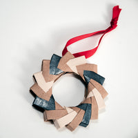 A handmade origami Christmas wreath in slate, cream and tan textured Japanese origami paper, and topped with red ribbon, made at NiMi Projects UK. 